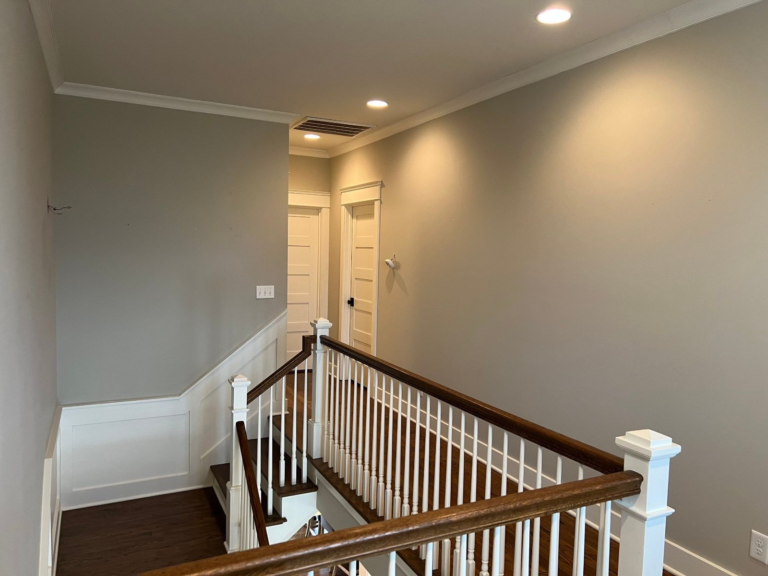 Upstairs hallway with fresh greige walls, white wainscoting and stair rail