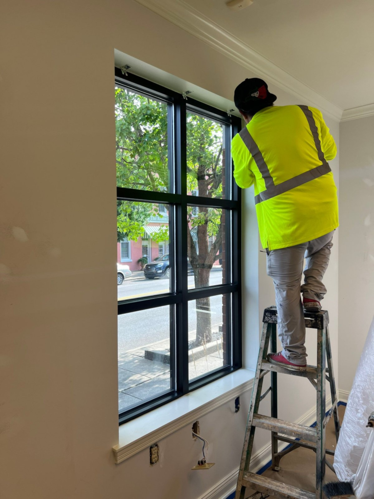 Painter on a ladder finishing window trim in a storefront office